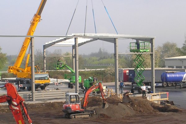 Eine Baustelle mit einem gelben Autokran im Hintergrund und einem kleinen roten Bagger im Vordergrund