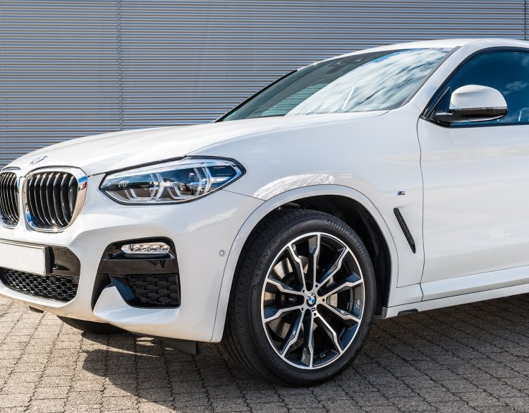glänzender, weißer BMW x4, der vor einer Halle steht.
