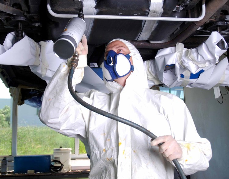 Wohnmobil wird mit einer Unterbodenversieglung besprüht von einem Mann im Schutzanzug.